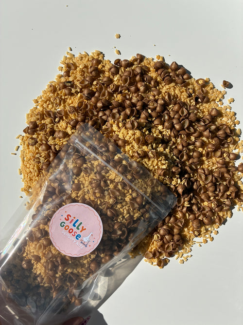 A clear stand-up pouch with a round pink 'Silly Goose' sticker, filled with dried pasta and rice. Sensory filler titled 'Cookie Crumble'
